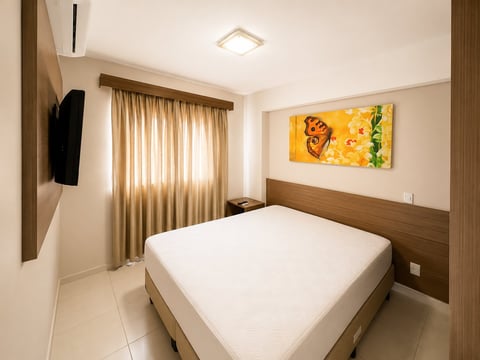 Modern bedroom with white bed, wood headboard, beige curtains, yellow floral artwork, and minimalist decor