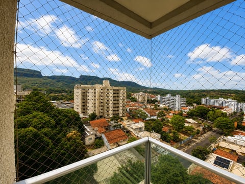 View from a high-rise balcony with safety net overlooking a suburban neighborhood with residential buildings and green hills under blue sky
